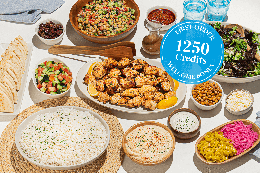 A spread of various dishes including grilled chicken, salads, rice, and hummus, with a blue circle reading 